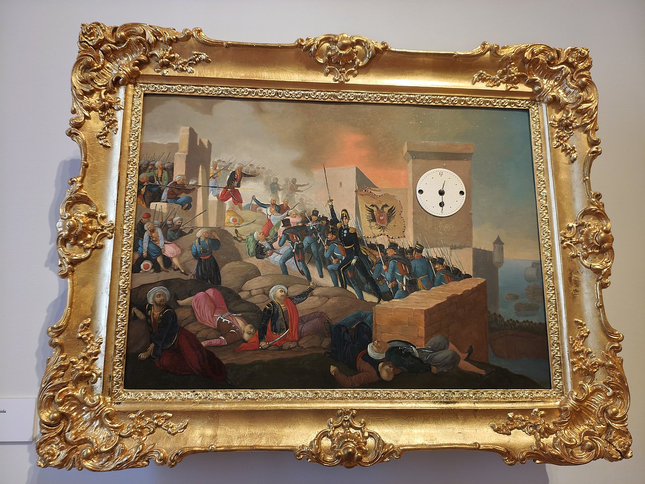 Das Bild zeigt das Gemälde mit dem Titel Bilderuhr: Erstürmung von Saida am 26. September 1840, mit Goldrahmen und ins Bild eingebauter Uhr.