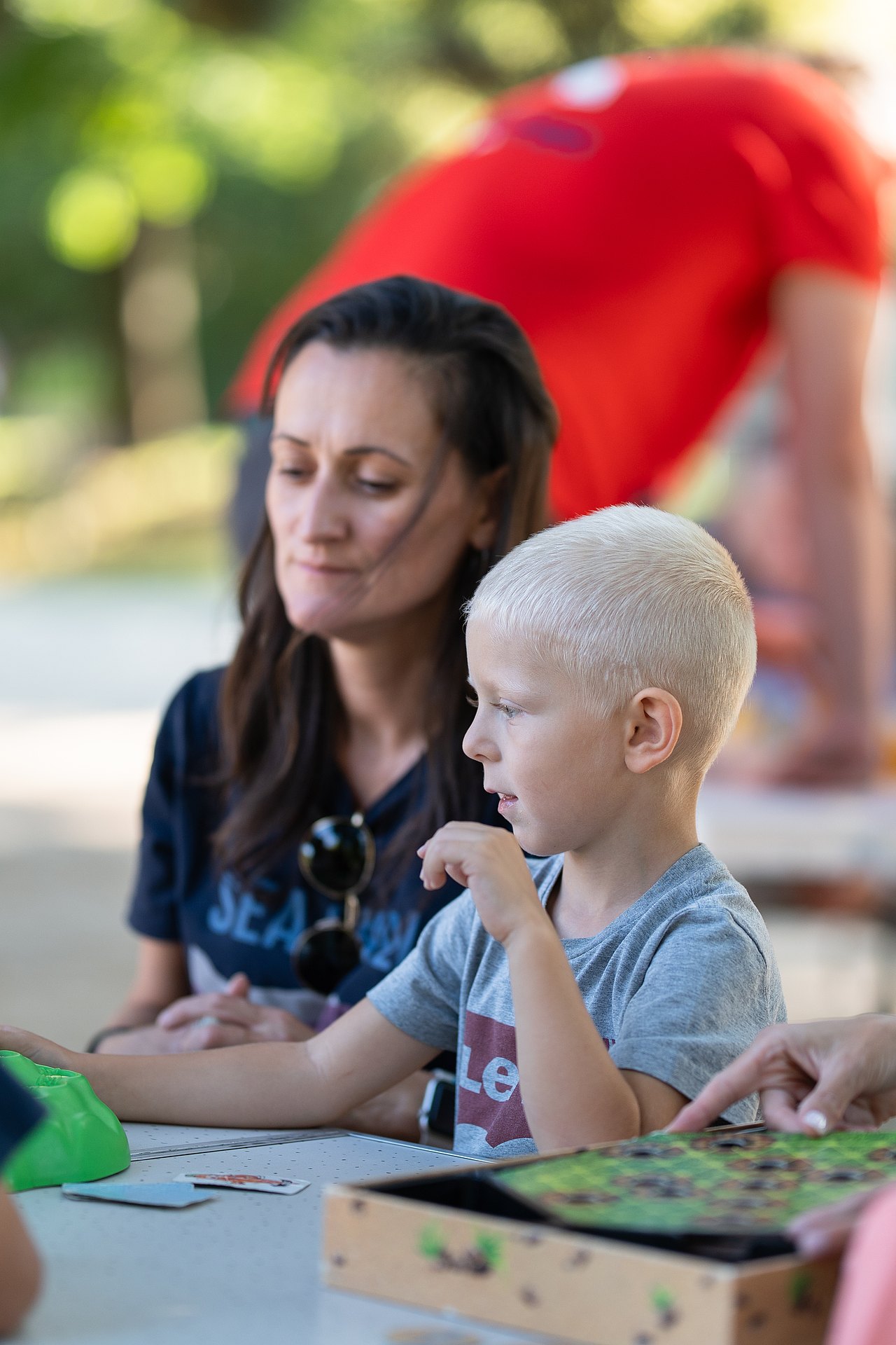 Frau und Kind an einem Spieltisch mit einem Brettspiel im Park