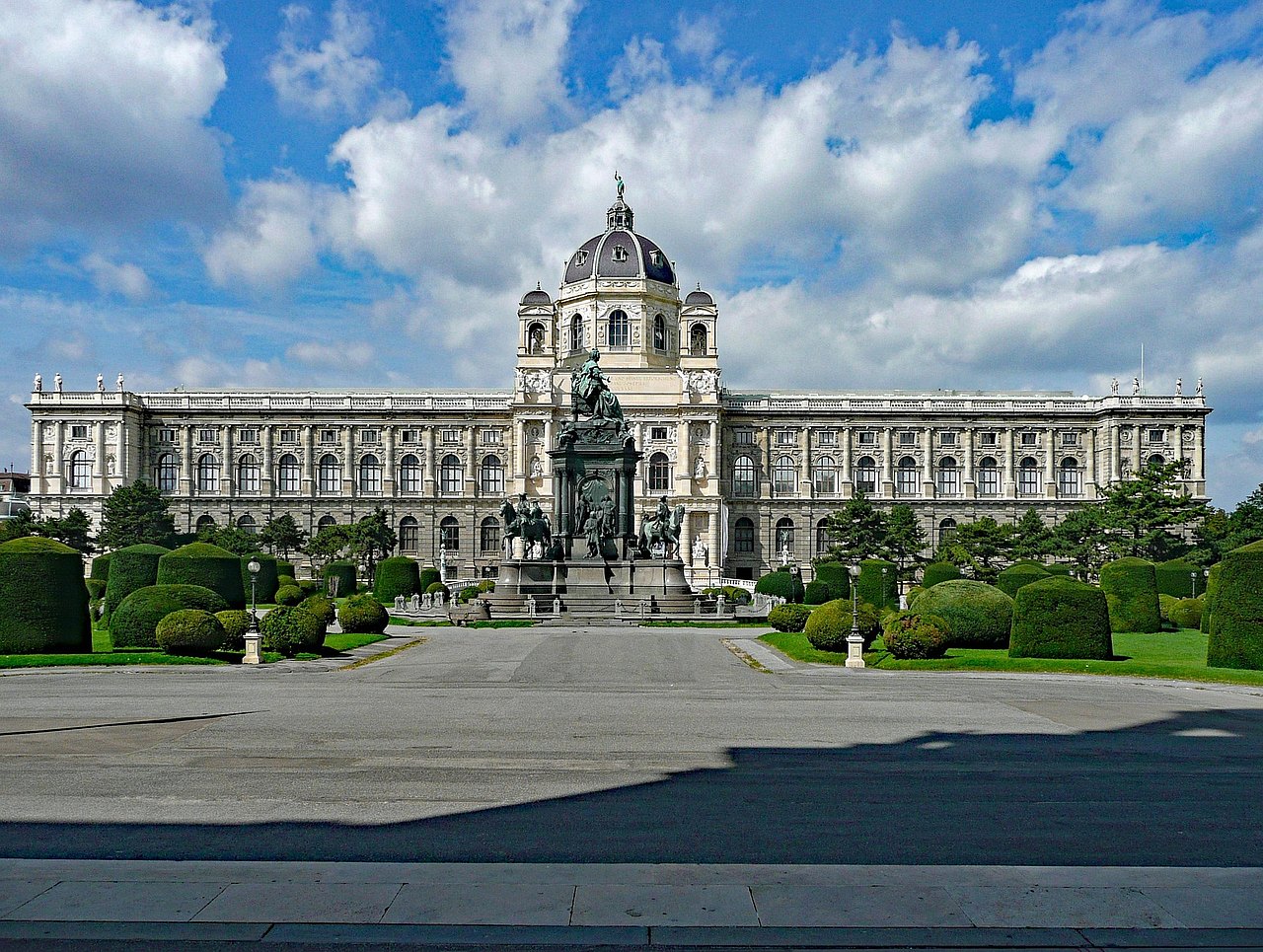 NHM Das Naturhistorische Museum ist frontal im Hintergrund zu sehen. Davor befinden sich die Grünflächen des Maria-Theresien-Platzes und die Maria-Theresien-Statue in der Mitte.