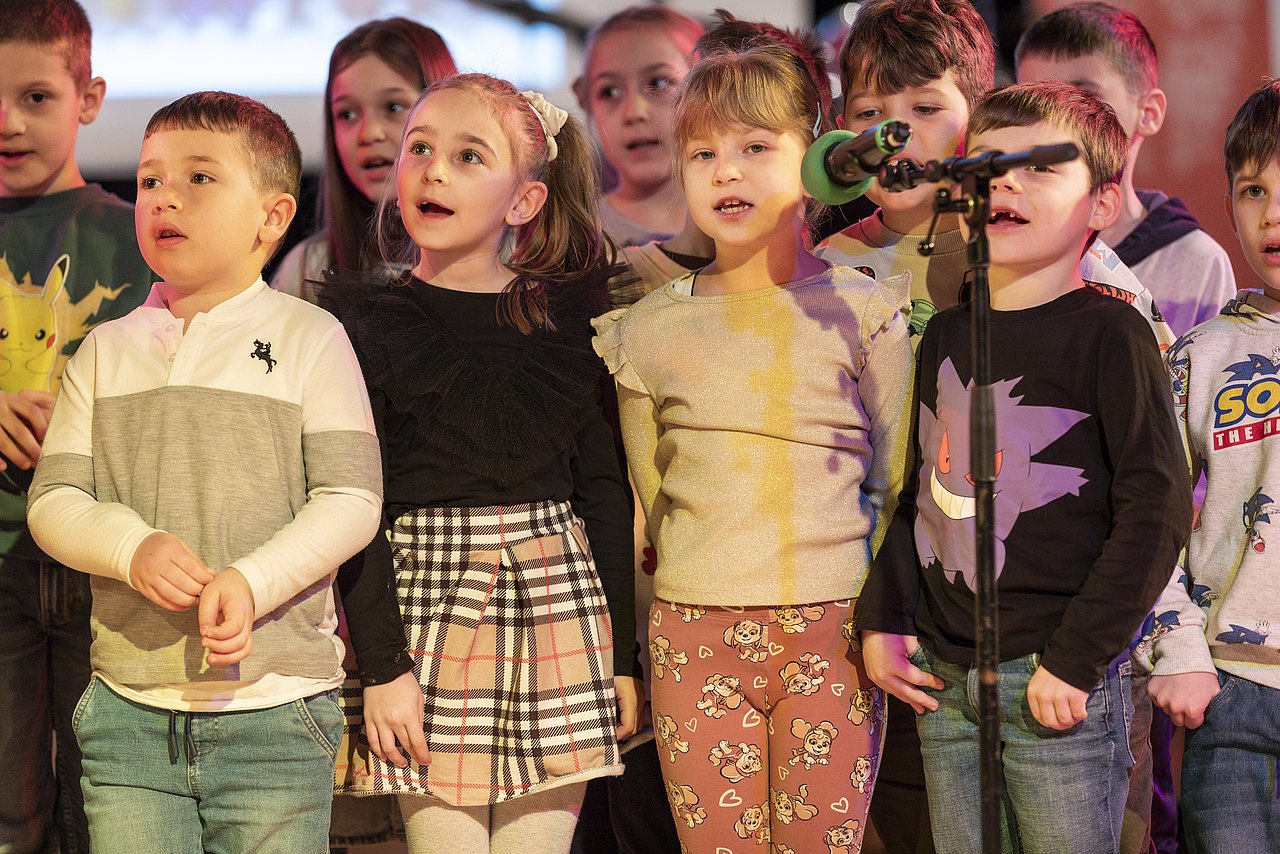Kinder stehen vor einem Mikrofon und singen