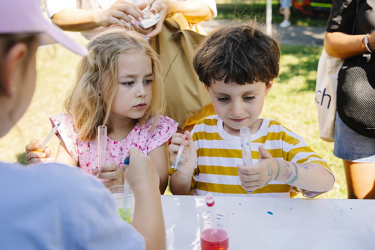 Bub und Mädchen mit Proberöhrchen bei Spielstation