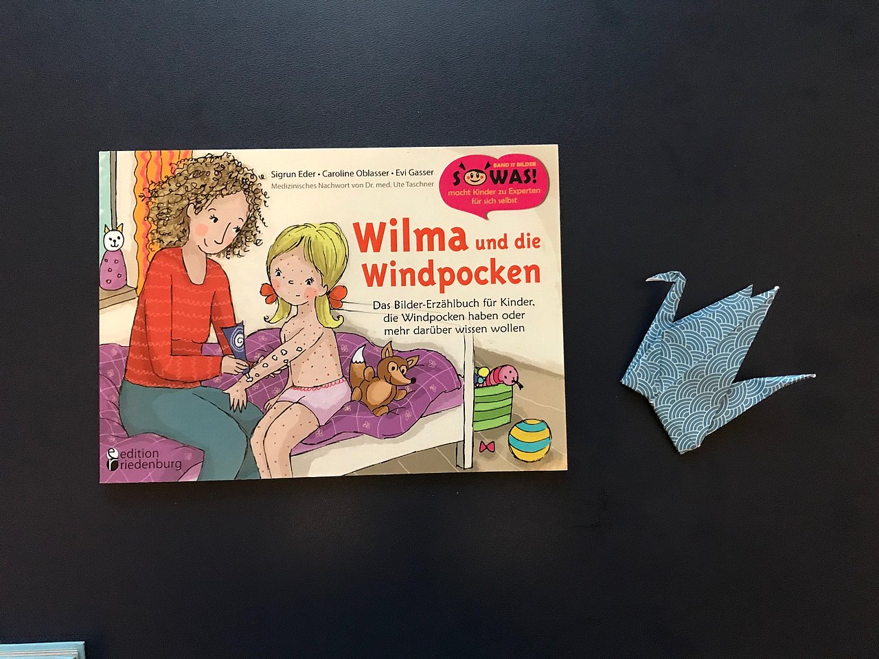 Buch "Wilma und die Windpocken" von Sigrun  Eder, Caroline Oblasser und Evi Gasser, daneben ein Papierkranich.