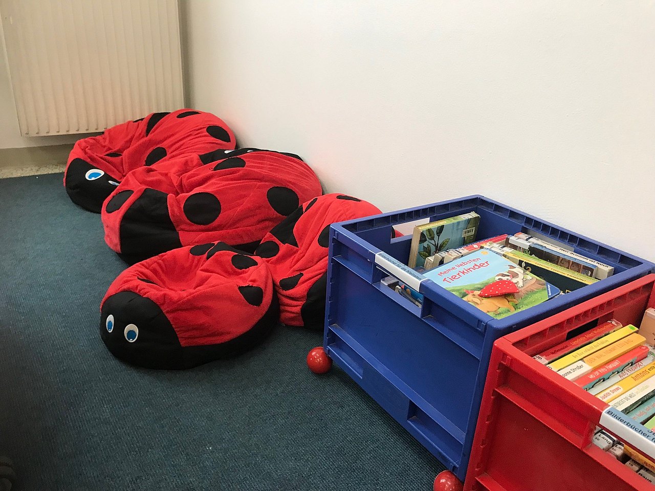 Vier Marienkäfer-Sitzsäcke, daneben zwei bunte Rollkisten mit Kinderbüchern.