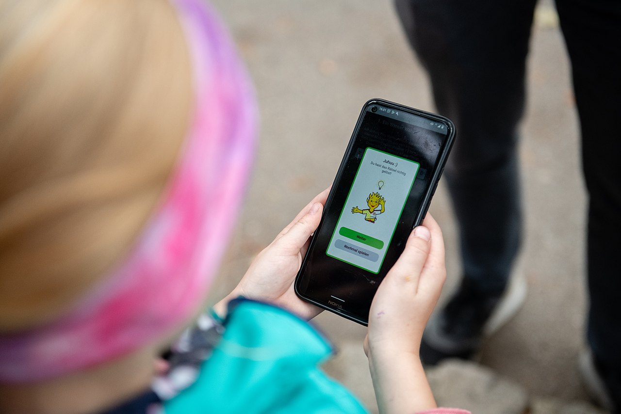 Kind schaut unterwegs auf einem Smartphone in die Kinderaktiv App