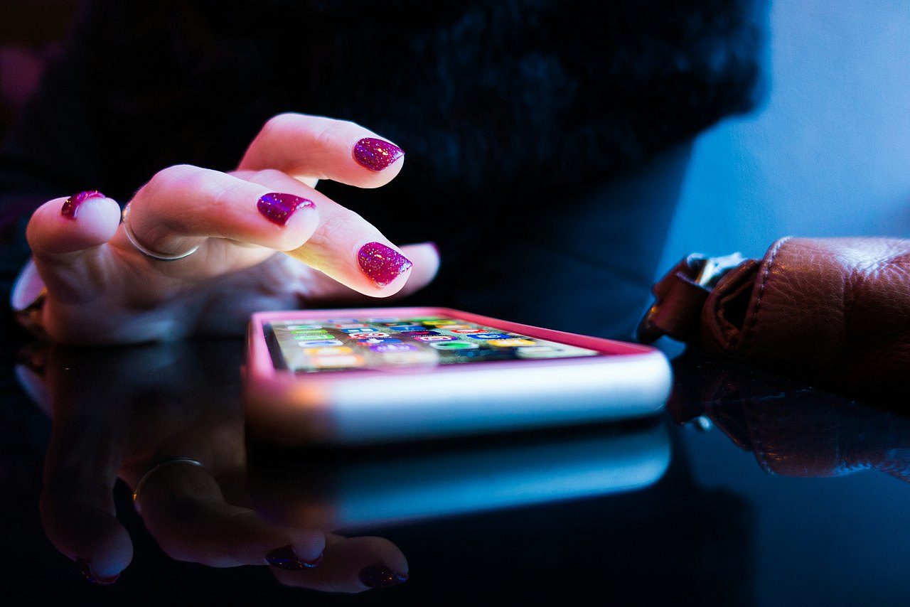 Rob Hampson via Unsplash Person mit pinken Fingernägel nutzt ein Smartphone mit grauer Hülle