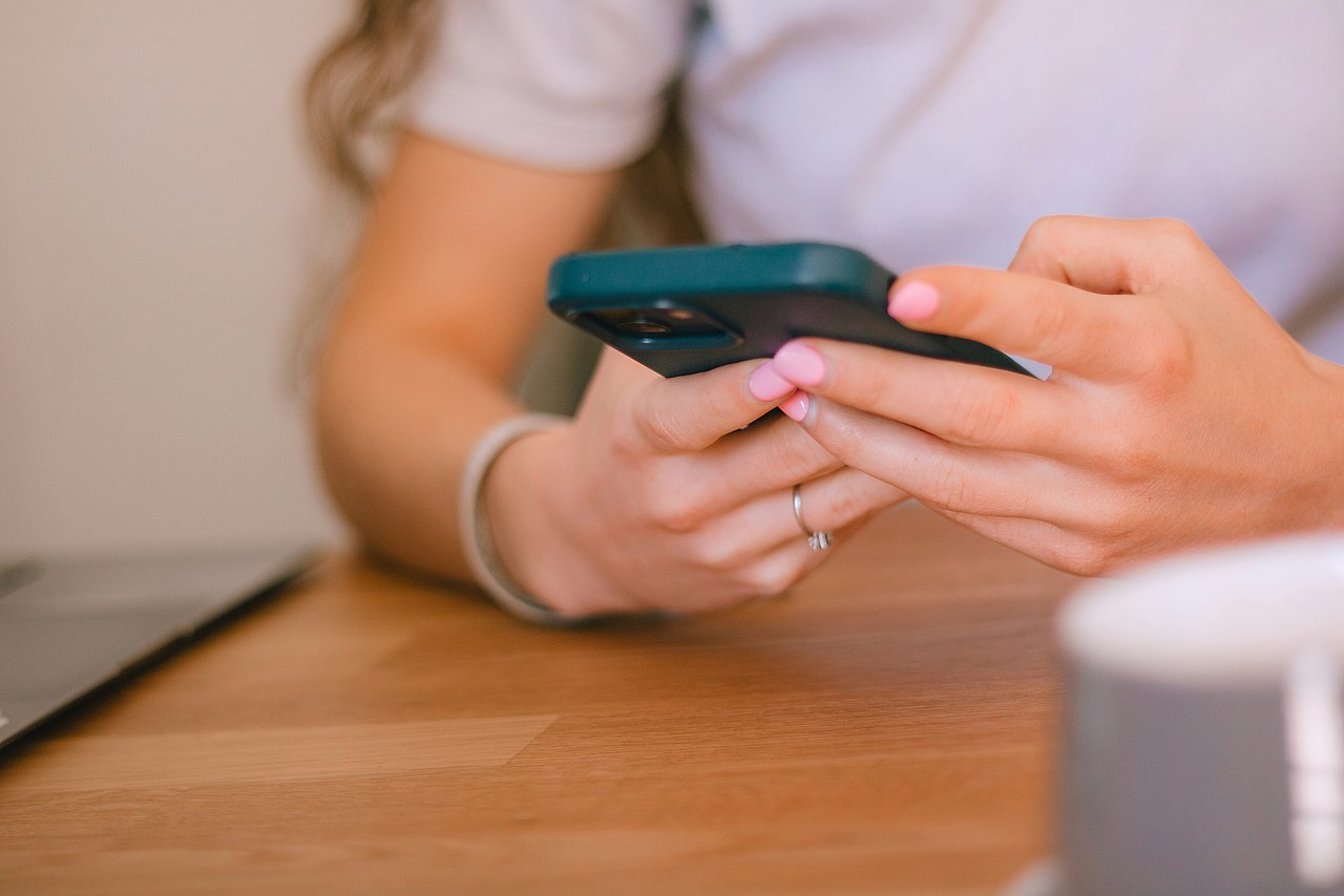Eine Person mit rosa Fingernägel benutzt ein Smartphone.