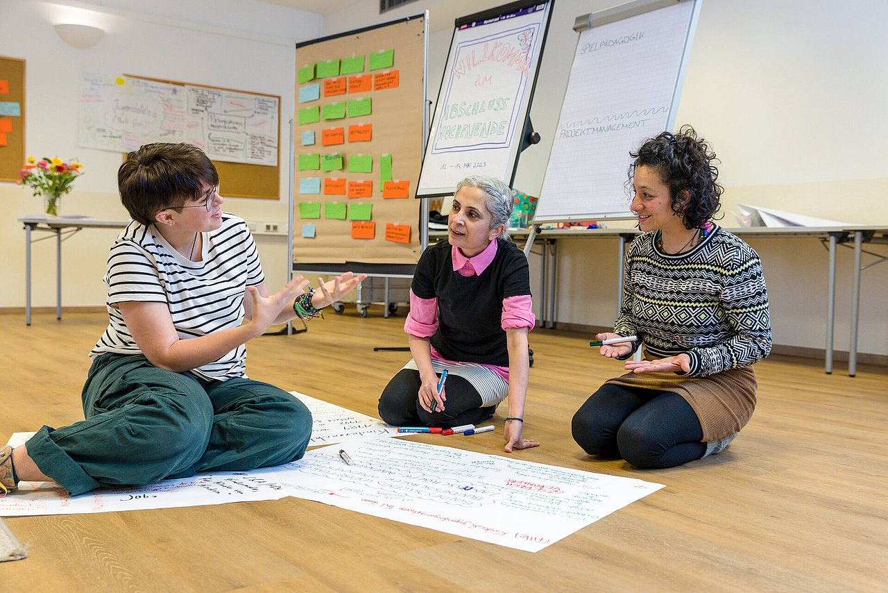 Drei Personen, die am Boden sitzen und angeregt diskutieren