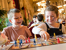 Zwei lachende Kinder spielen ein Brettspiel im Festsaal des Rathauses 