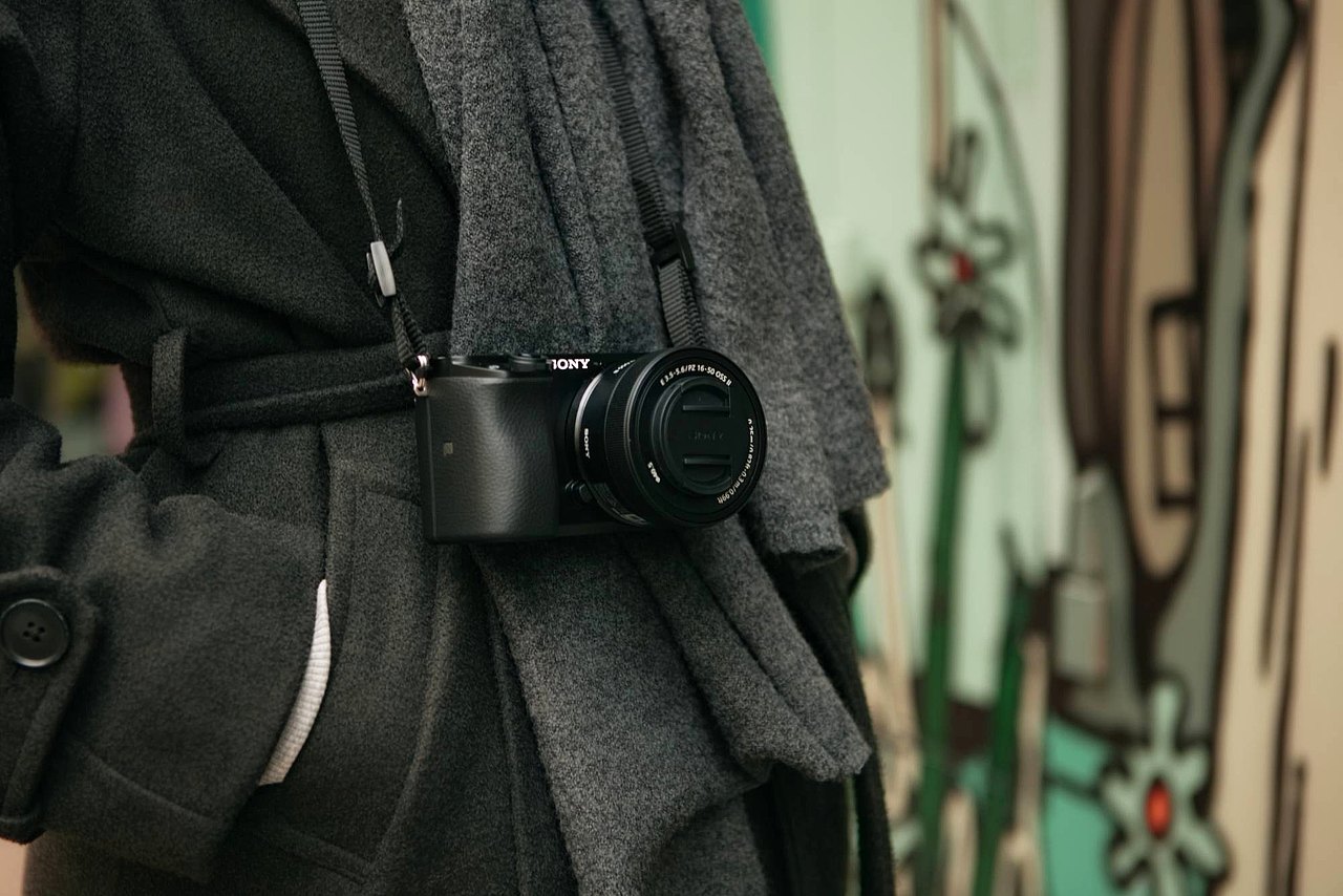 Eine Jugendliche trägt eine kleine Sony-Kamera am Tragegurt, die seitlich an ihrer Hüfte hängt.