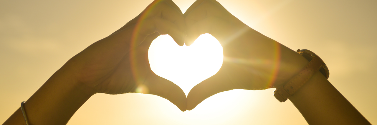 Zwei Hände die mit den Fingern ein Herz Richtung Himmel und Sonne formen 