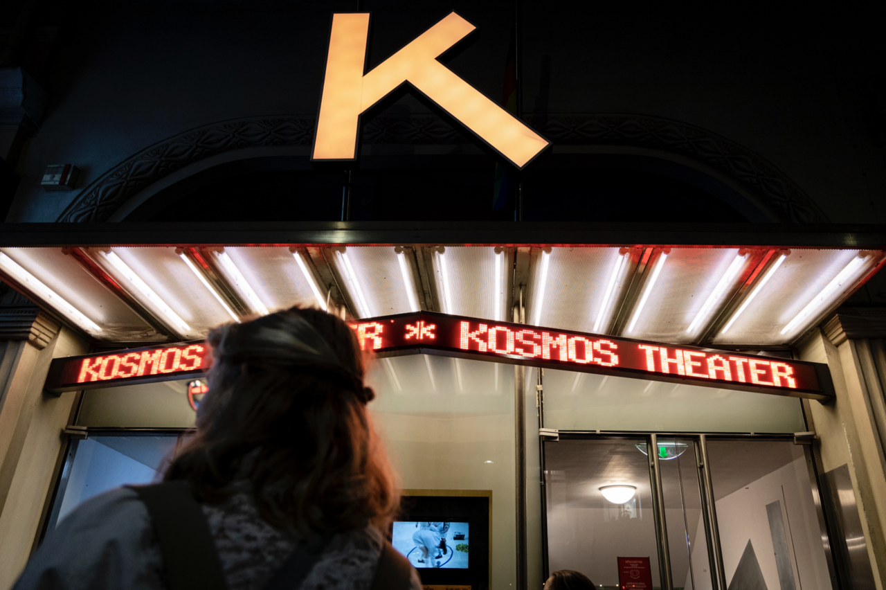 Eine junge Frau von hinten, wie sie auf das Kosmos Theater blickt