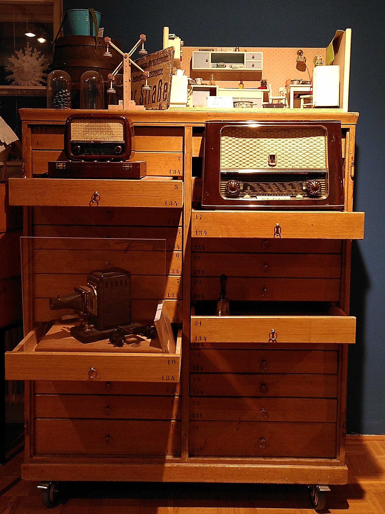 Ein altern Holz-Schubladen-Kasten mit zwei vintage Radios, einer vintage Kamera und einer selbstgebauten Puppenküche aus den 1950ern.