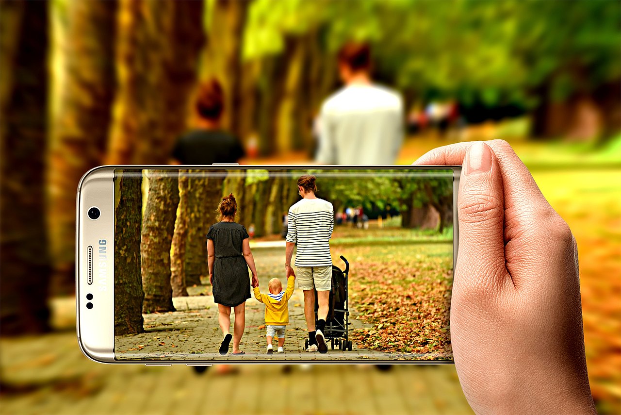 Mann , Frau und Kind inherbstlicher Landschaft im Vordergrund durch ein Handy betrachtet