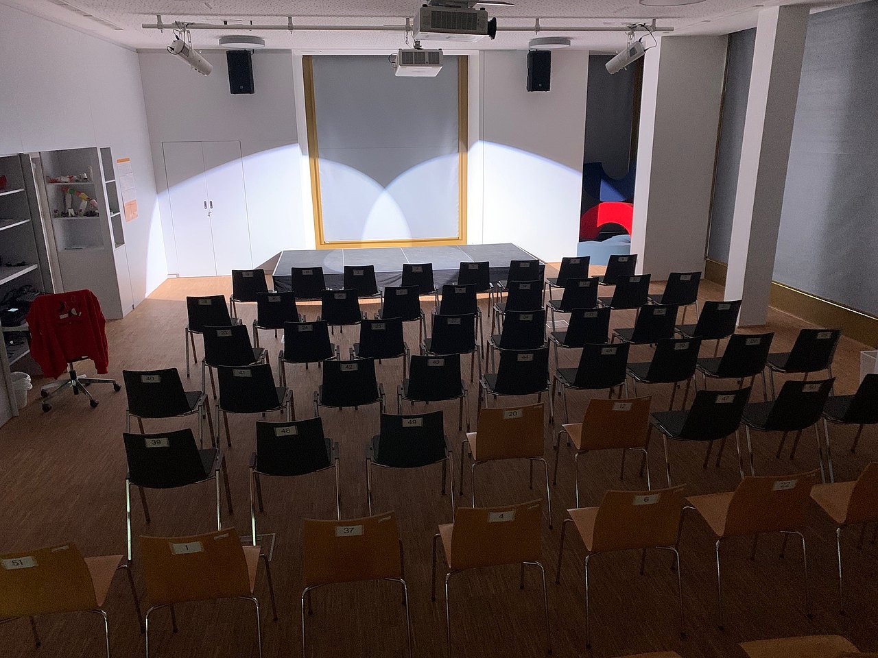 Raum mit Bestuhlung, Bühne und Scheinwerferlicht