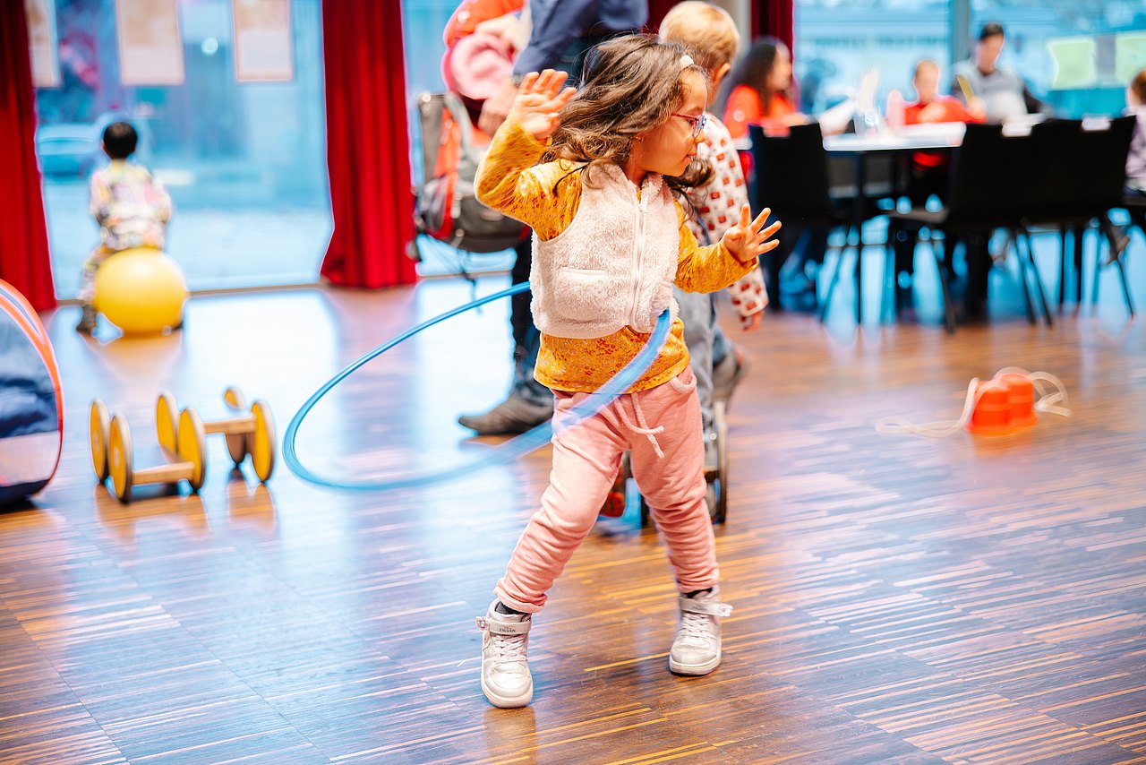 Kind mit Hula Hoop Reifen mit verschiedenen Spielzeugen am Boden