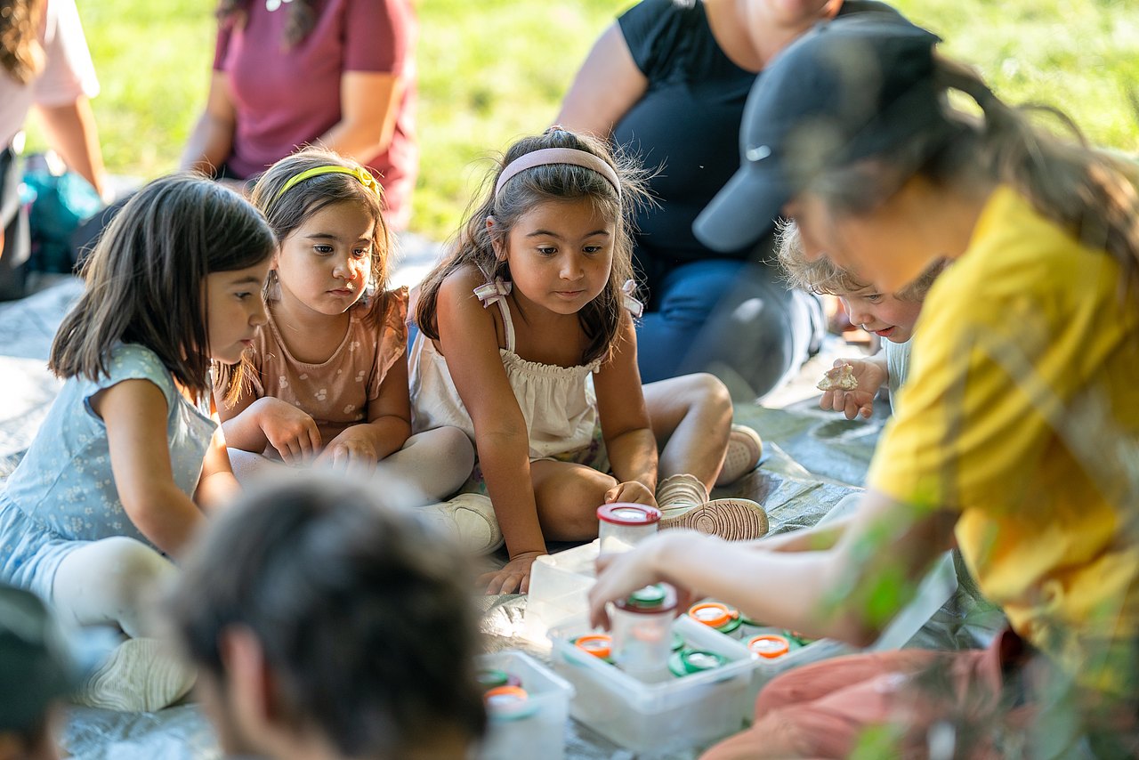 Kinder sitzen mit Becherlupen in der Wiese