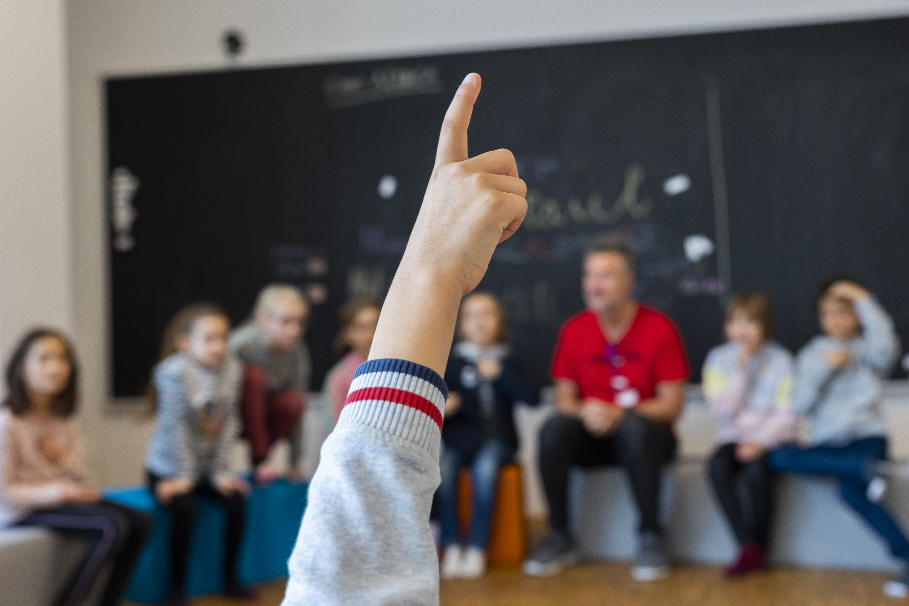 Kind zeigt auf, dahinter sitzen weitere Kinder