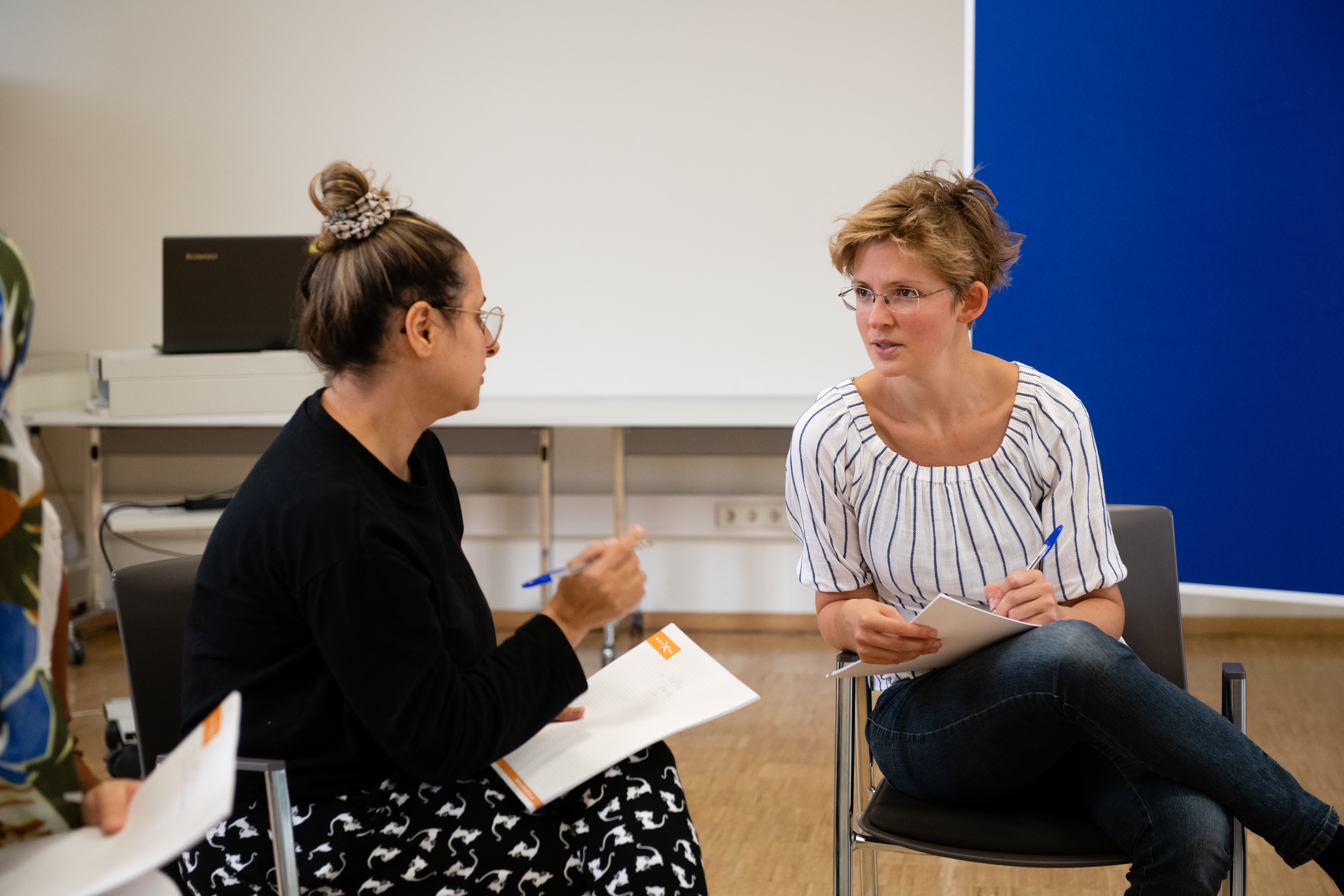 Zwei Frauen sitzen in einem Seminarraum und sprechen miteinander.