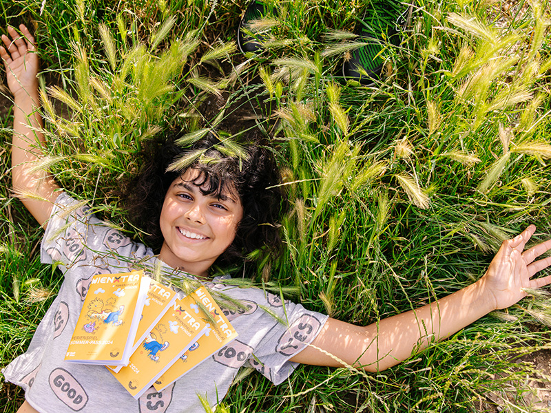 Ein Mädchen liegt im hohen Gras und freut sich auf die erholsamen Sommerferien.