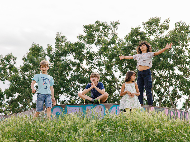 Vier Kinder stehen auf einem Hügel umgeben von hohem Gras und Bäumen und freuen sich auf den Sommer.